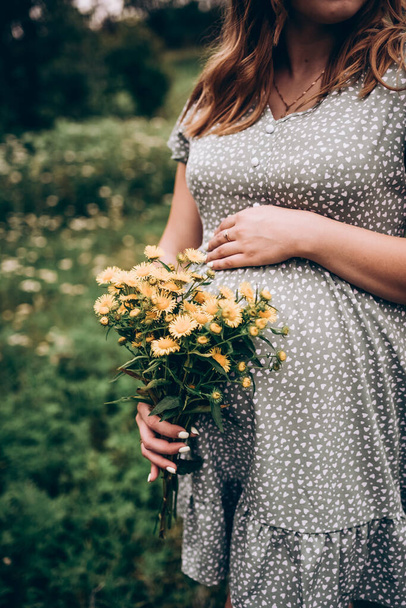 Těhotné břicho zblízka v zelených tónech a květinách. Těhotná žena a budoucí matka - Fotografie, Obrázek