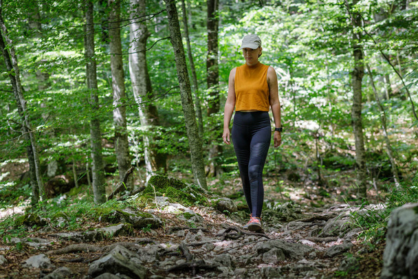 Young sporty woman walking on trail in the forest - Фото, зображення