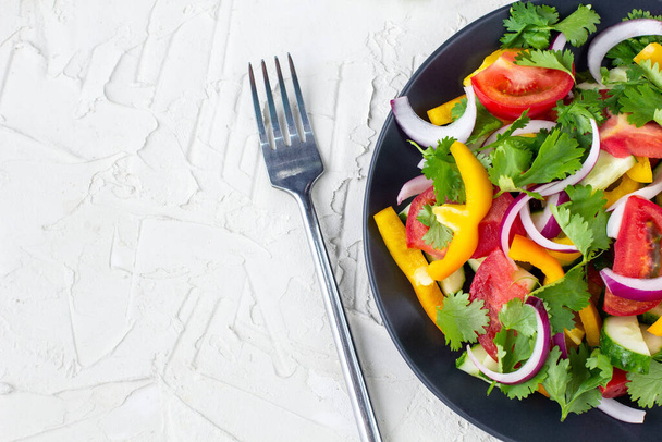 Assiette de salade arc-en-ciel avec différents légumes et herbes sur assiette noire avec fourchette sur fond de pierre blanche. Vue de dessus avec copyspace - Photo, image