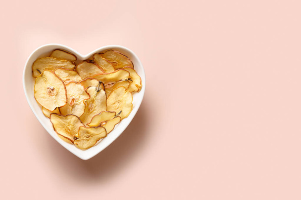Fruits pear chips in plate shaped of heart on a pink background. - Фото, зображення