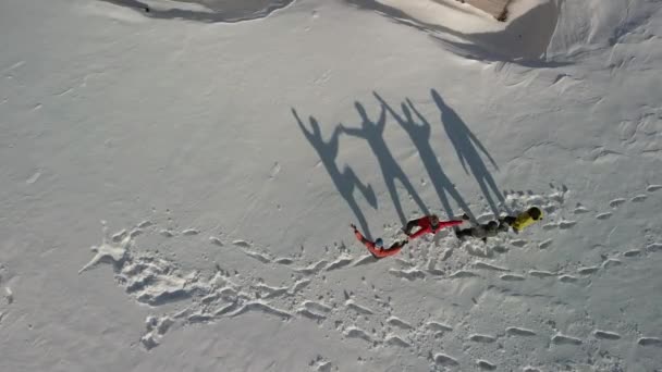 Cuatro viajeros bailan y muestran diferentes figuras divertidas que reflejan una gran sombra sobre la nieve blanca. Vista aérea de grandes sombras. - Imágenes, Vídeo