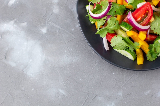 Egy tányér szivárvány saláta különböző zöldségekkel és gyógynövényekkel fekete tányéron szürke kő alapon. Felülnézet másoló felülettel - Fotó, kép