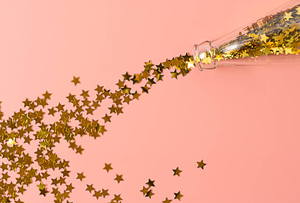 zlaté konfety hvězdy, jako by šampaňské vylil ze skleněné láhve na růžové pozadí, horizontální abstraktní obraz na pozadí, novoroční party koncept, okouzlující Vánoce pro dívky - Fotografie, Obrázek