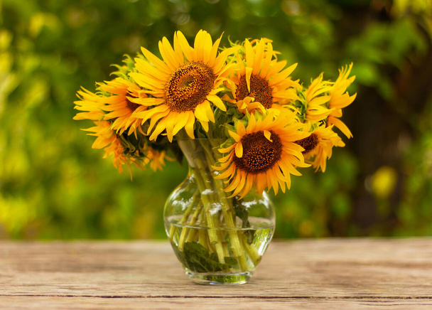 bouquet of beautiful yellow sunflower flowers in a glass vase on an old rustic wooden table in the garden - 写真・画像