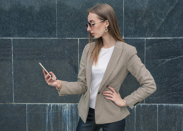 Красива молода мода стильна жінка з мобільним телефоном на стіні міського фону
 - Фото, зображення