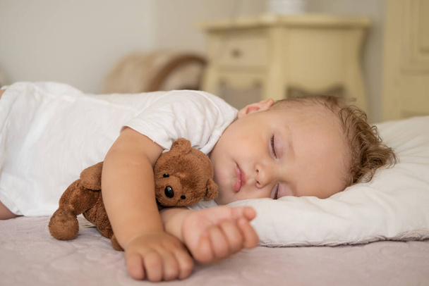funny baby boy sleeping on bed at home. child hugging teddy bear.  - 写真・画像
