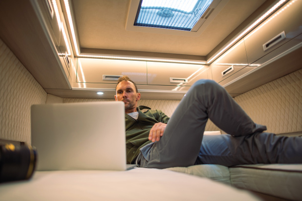 Blanke mannen liggen in zijn camper Van Bed in de voorkant van zijn laptop computer en kijken naar zijn favoriete online filmservice.  - Foto, afbeelding