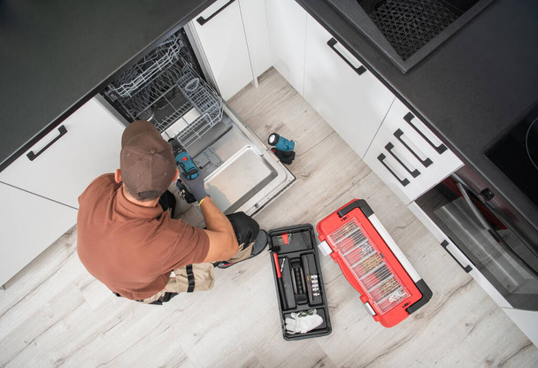 Technician Worker in His 40s Installing Dishwasher Inside Residential Apartment Kitchen. Home Appliances Theme. - Photo, Image