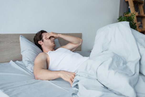 fiatal férfi eltakarja a szemét kézzel, miközben fekszik az ágyban - Fotó, kép