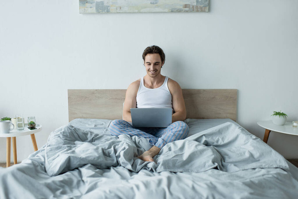 smiling man sitting in bed and using laptop  - Photo, Image