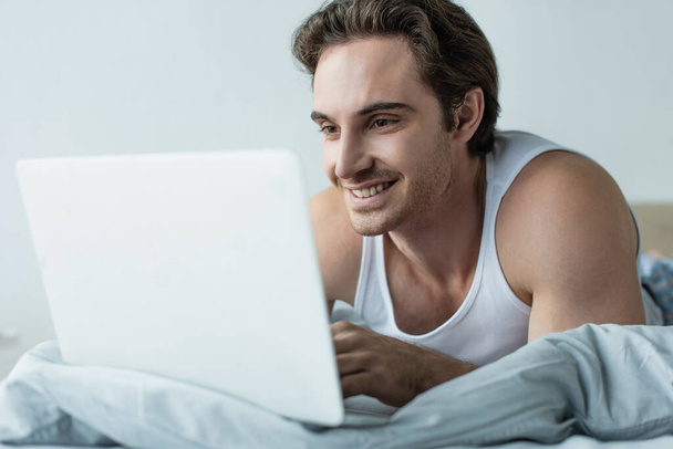 szczęśliwy młody człowiek patrząc na laptopa w łóżku - Zdjęcie, obraz
