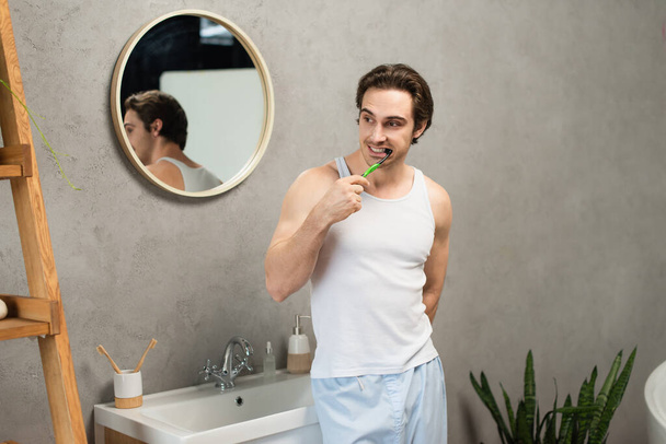 man in white tank top brushing teeth near sink in bathroom - 写真・画像