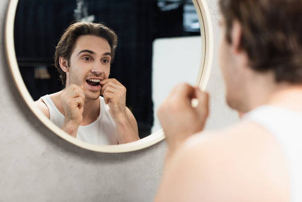young man flossing teeth near mirror in bathroom - Fotó, kép