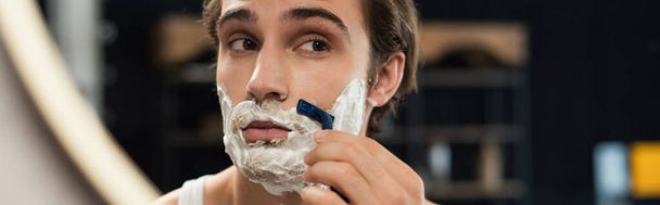 young man shaving near mirror with safety razor, banner - 写真・画像