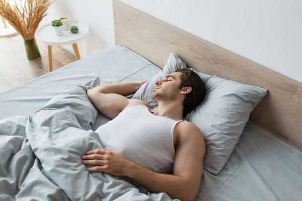young brunette man sleeping in bed under blue blanket - Photo, Image