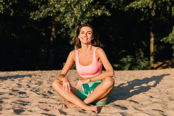 Вмістити спортивну жінку в ідеальній формі на заході сонця на міському пляжі в йозі позують спокійні щасливі позитивні емоції
 - Фото, зображення