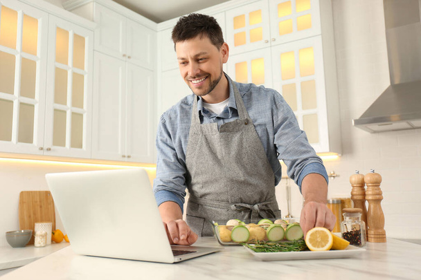 Man making dinner while watching online cooking course via laptop kitchen - 写真・画像