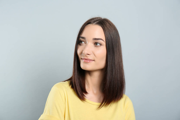 Portrait of pretty young woman with gorgeous chestnut hair on light grey background - Zdjęcie, obraz