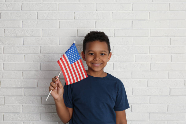 Happy African-American boy holding national flag near white brick wall - Fotó, kép