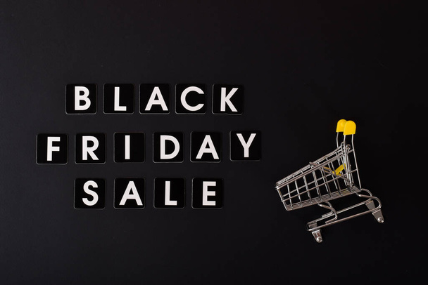 On a black background, the inscription Black Friday sale and a stroller from the supermarket. Flat layout, top view - Foto, Bild