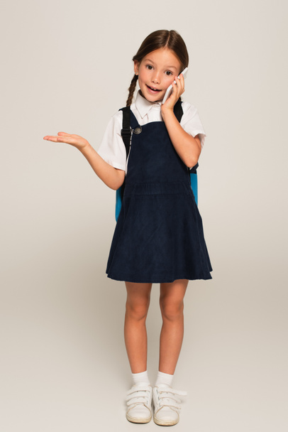 schoolgirl talking on cellphone and pointing with hand on grey - Photo, Image