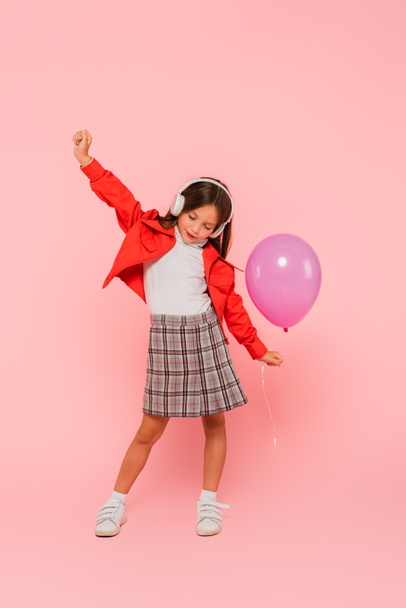 trendy child with balloon dancing in headphones on pink - Photo, Image