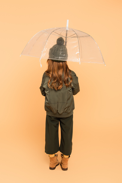 back view of trendy girl standing under transparent umbrella on beige - Foto, Bild