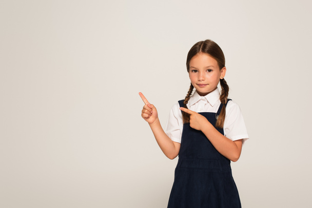 girl in school uniform pointing with fingers isolated on grey - Foto, immagini