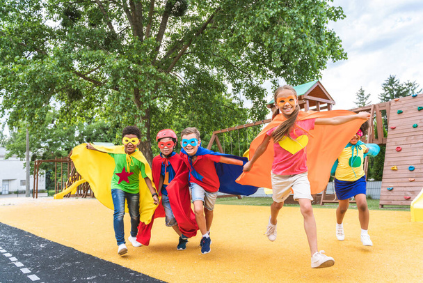 Multiracial group of young schooler wearing superhero costumes and having fun outdoors - Valokuva, kuva