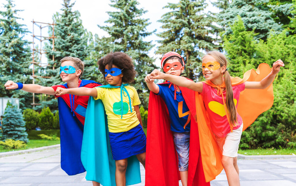 Groupe multiracial de jeunes écoliers portant des costumes de super-héros et s'amusant à l'extérieur - Photo, image