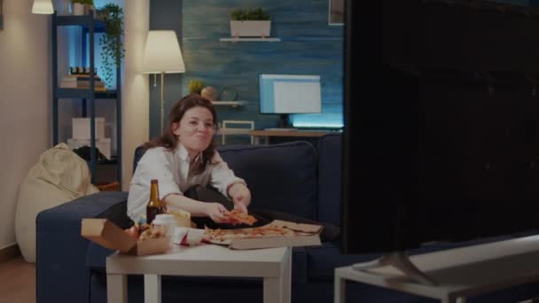 Osoba jedząca kawałek pizzy podczas oglądania komedii w telewizji - Materiał filmowy, wideo