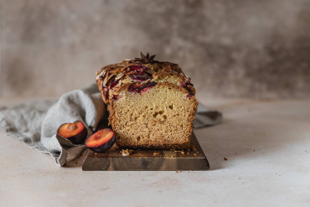 Homemade spicy plum cake decorated with almond on a wooden serving board, concrete background. Loaf cake with plum, spices and almond. - Foto, immagini
