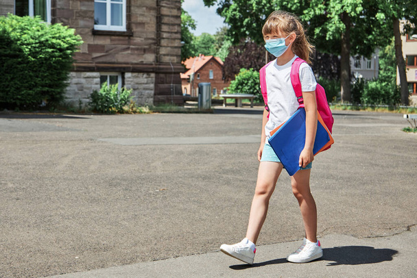 La niña va a la escuela con una mochila y una máscara médica protectora. Comienzo del año escolar, regreso a la escuela. Nueva realidad en medio de un virus - Foto, Imagen