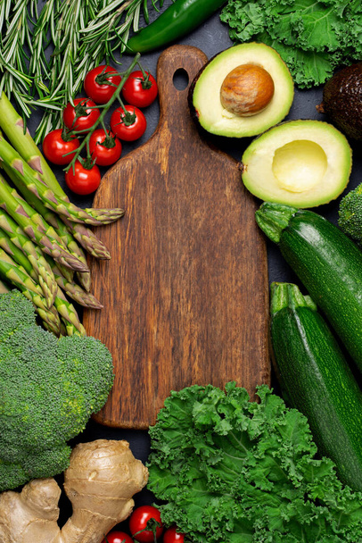 Healthy fresh green vegetables and herbs around wooden cutting board for paleo diet. - Zdjęcie, obraz