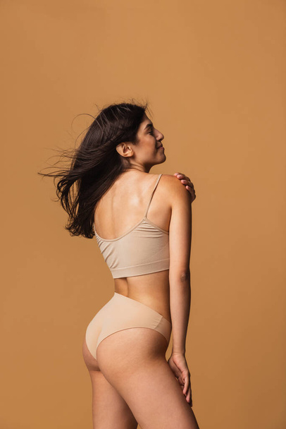 Back view of sportive body of young caucasian woman isolated on brown studio background. Natural beauty concept - Foto, imagen