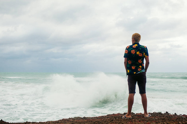 Man standing on the edge of the abyss facing to the sea with big waves - Fotoğraf, Görsel