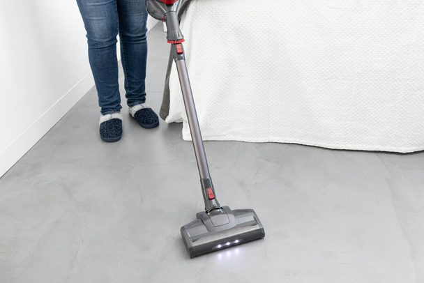 Woman cleaning with a cordless vacuum cleaner in a modern bedroom. Copy space - Photo, Image
