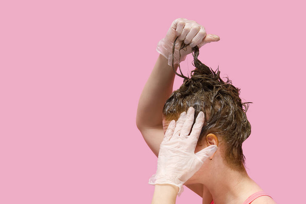 Home beauty industry in coronavirus pandemic time. young woman in gloves stays at home and painting her hairs - Fotoğraf, Görsel