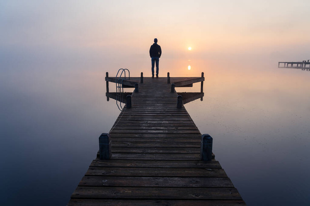 Silhouette d'un homme regardant le lever du soleil sur un matin brumeux et tranquille. - Photo, image