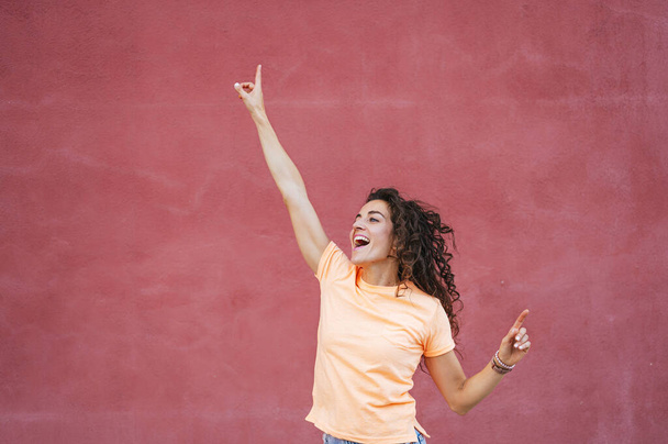 Veselá žena tančí s rukama zvednutýma před stěnu - Fotografie, Obrázek