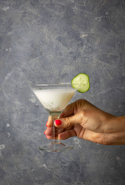Айран с укропом в бокале мартини со свежим огурцом в руке женщины - Фото, изображение