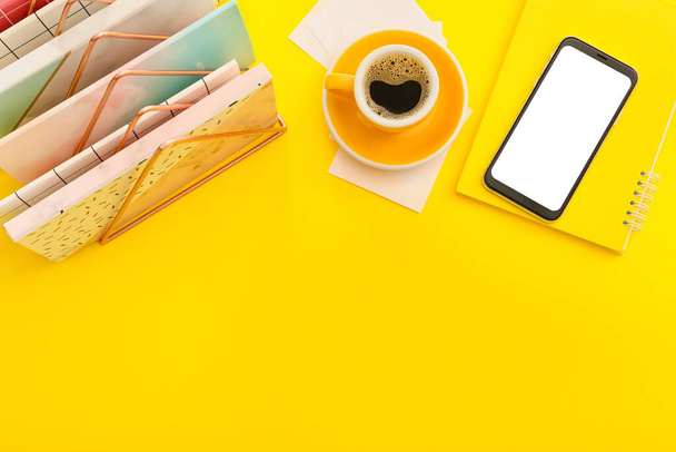 Мобильный телефон с ноутбуками и чашкой кофе на цветном фоне - Фото, изображение