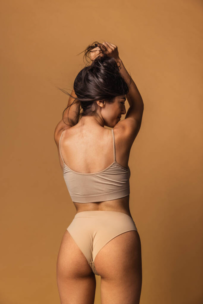 Back view of sportive body of young caucasian woman isolated on brown studio background. Natural beauty concept - Φωτογραφία, εικόνα