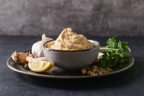 Bowl with tasty hummus and ingredients on dark background - Photo, Image