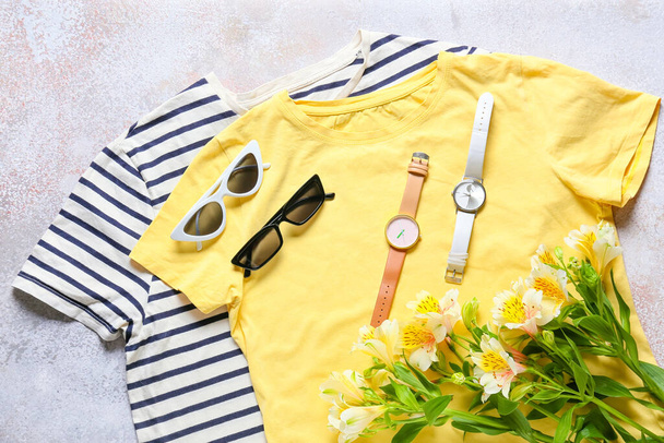 Композиция со стильными футболками, солнцезащитными очками, наручными часами и цветами на светлом фоне - Фото, изображение