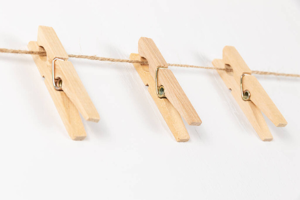 τρία ξύλινα μανταλάκια με μεταλλικό ελατήριο κρεμασμένα σε σχοινί σε λευκό φόντο. επιλεκτική εστίαση - Φωτογραφία, εικόνα