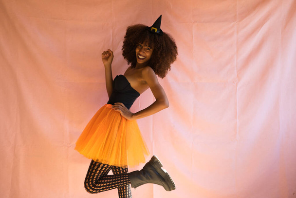 young african american woman dressed as a witch for halloween party. She wears a witch hat and orange skirt. - 写真・画像