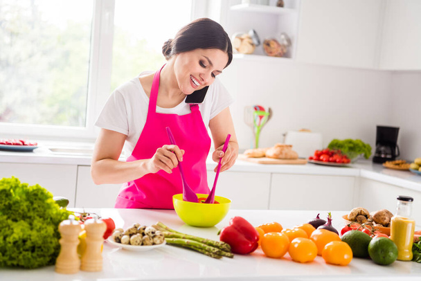 Foto portret vrouw in schort glimlachen koken vegetarische schotel praten op mobiele telefoon - Foto, afbeelding