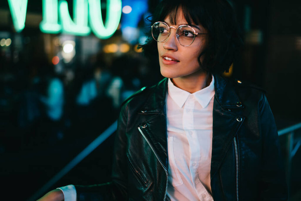 Dreamy gorgeous young woman with stylish short haircut and cool eyeglasses looking up standing outdoors on street, pondering trendy dressed hipster girl in eyewear thinking at metropolitan urbanity - Foto, Imagem