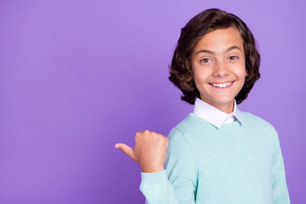 Photo of little funny brunet boy point empty space wear blue sweater isolated on purple background - Foto, imagen